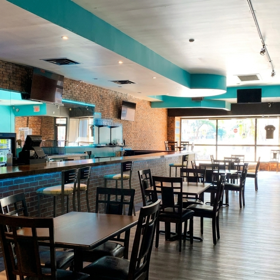 Bright modern restaurant dining room with brick walls, turquoise accents, bar counter, and neatly arranged tables and chairs.